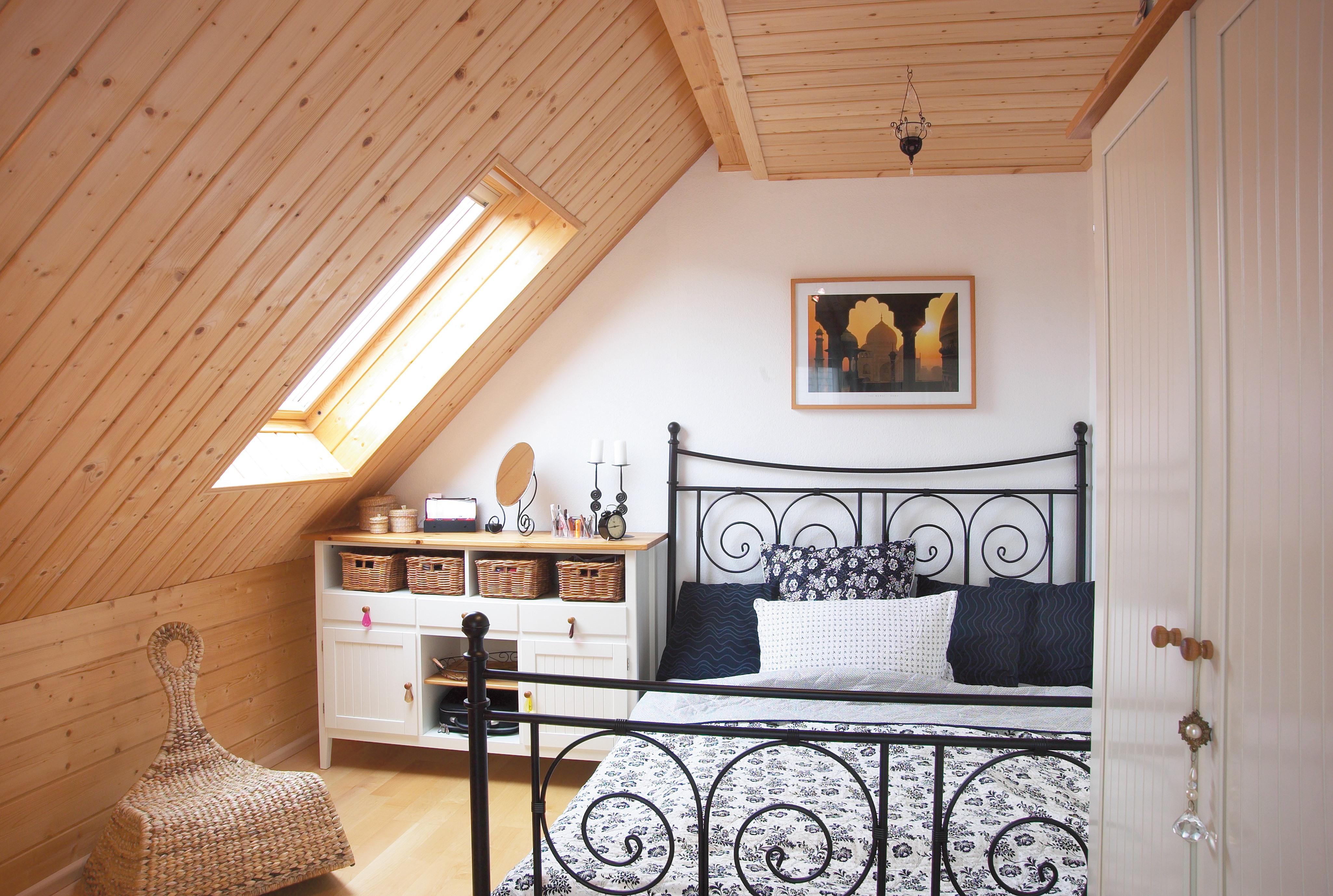 Schlafzimmer mit schrägen Holzpaneelen #dachschräge #bett #deckenpaneel #holzhaus #bettwäsche #kommode #schaukelstuhl #kleiderschrank #holzpaneel #wandpaneel ©Stommel Haus