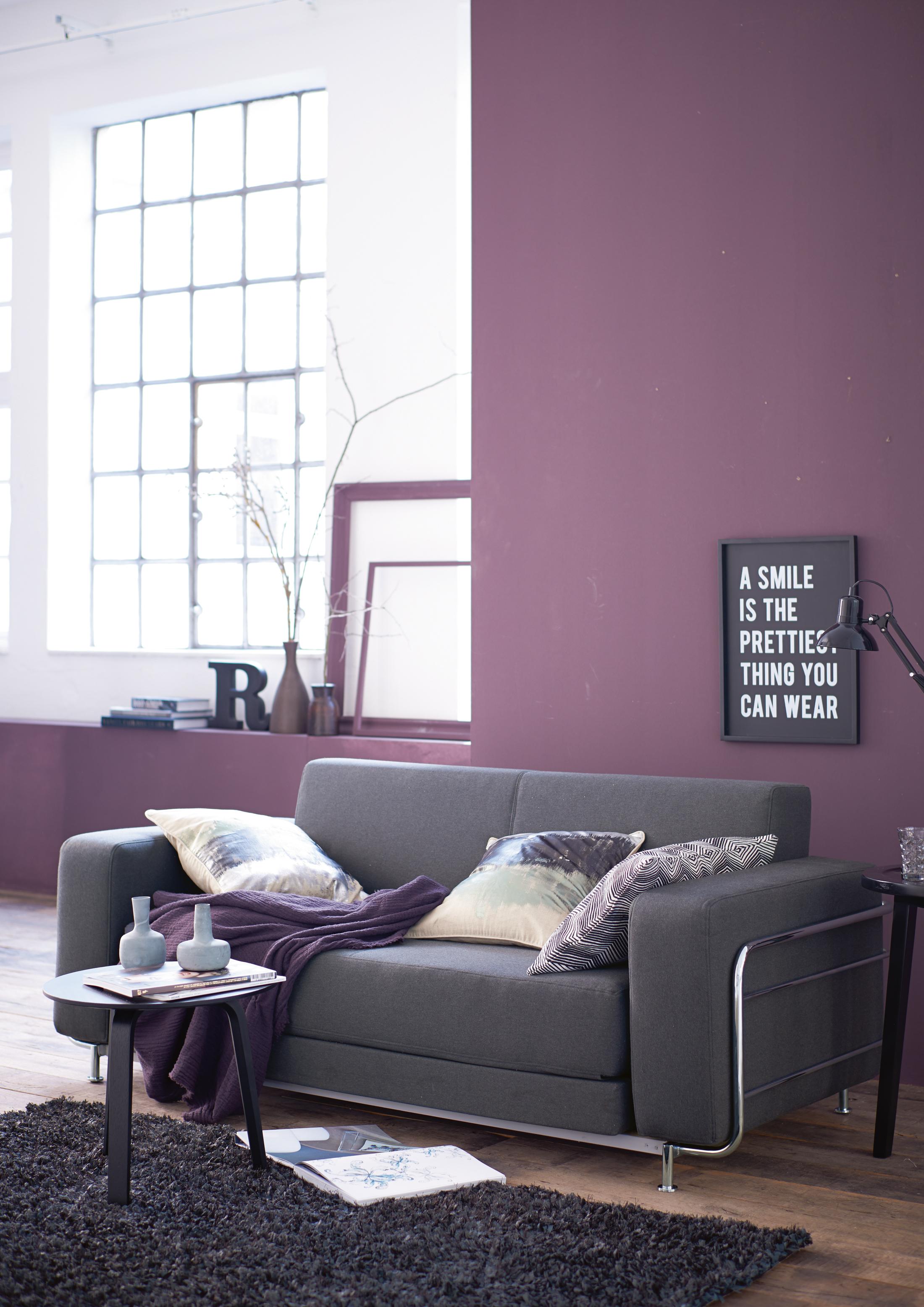 Graues Sofa vor lilafarbener Wand #couchtisch #beistelltisch #hocker #teppich #kissen #sofa #grauessofa #lilawandfarbe ©Impressionen