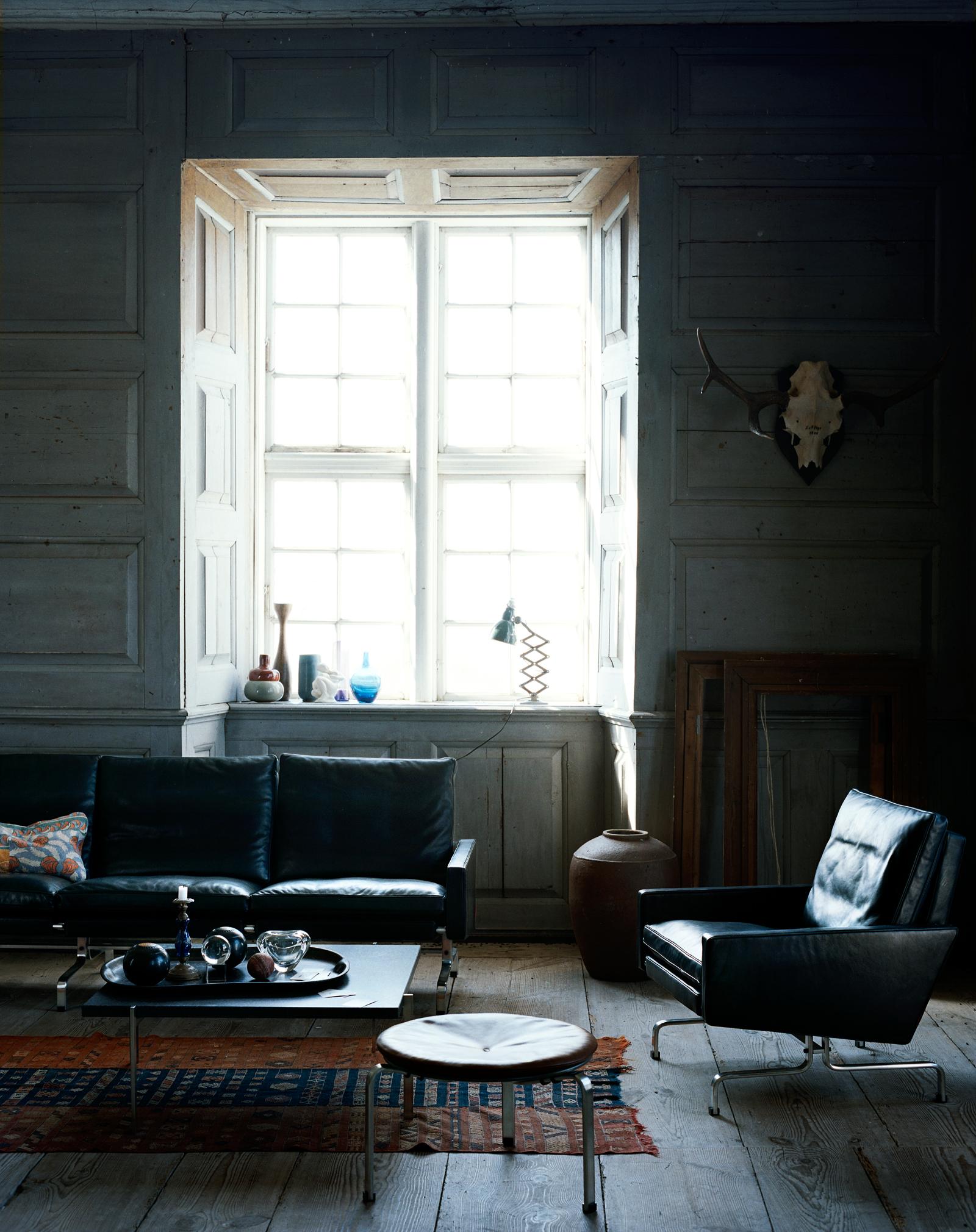 Wohnzimmer mit Sitzmöbeln aus schwarzem Leder #geweih #hocker #teppich #erkerfenster #schwarzesledersofa ©Fritz Hansen/Ditte Isager